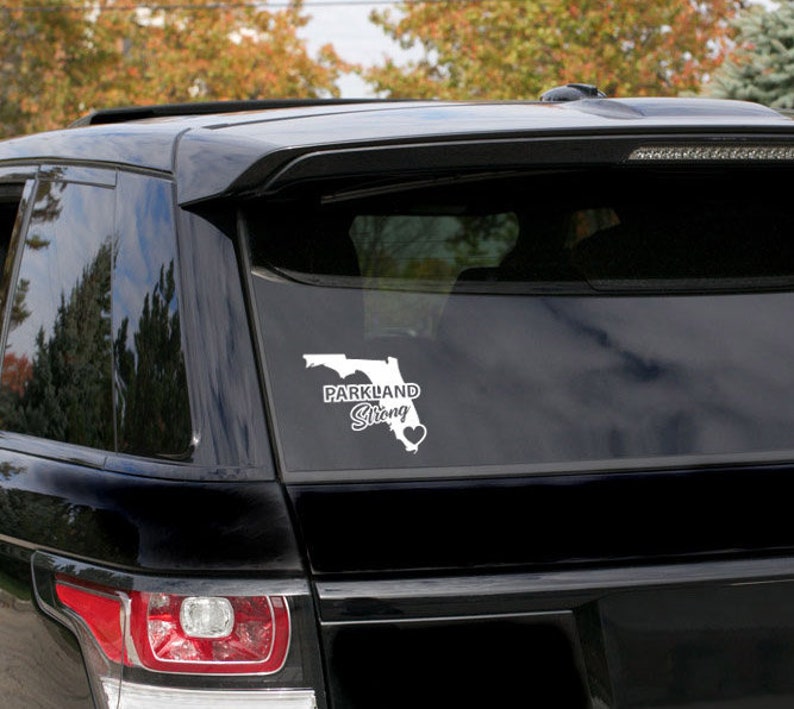May include: A black car with a white vinyl decal on the rear window. The decal features an outline of the state of Florida with the words "Parkland Strong" and a heart.