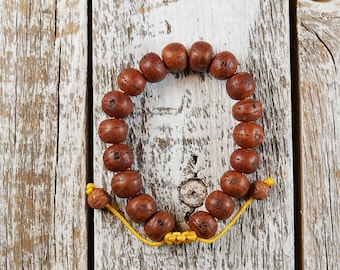 Puede incluir: Un brazalete de cuentas de madera marrón con un cierre de cuerda amarilla. Las cuentas son redondas y tienen un acabado de madera natural.