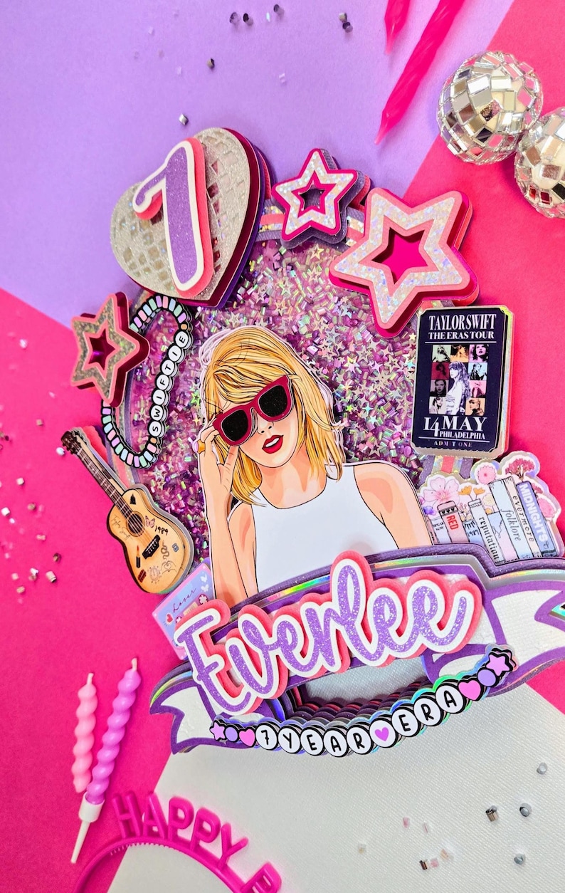 May include: A colorful cake topper with a Taylor Swift theme. It features a cartoon illustration of Taylor Swift wearing sunglasses, surrounded by stars, a guitar, and the text "Everlee". The topper includes the text "7 YEAR ERA" and a concert date.