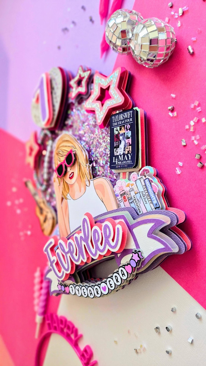 May include: A layered cake topper featuring a cartoon illustration of a blonde woman wearing pink sunglasses. The topper includes the text "Everlee" in purple, a concert poster, and star-shaped decorations. The color scheme is primarily pink and purple.