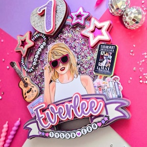May include: A colorful birthday cake topper featuring a cartoon illustration of a woman wearing sunglasses. The topper includes stars, a guitar, and the text "Everlee 7 Year Era". Pink and purple accents with glitter.