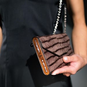 May include: A brown leather clutch purse with a wooden frame and a silver chain strap. The purse has a textured, striped pattern.