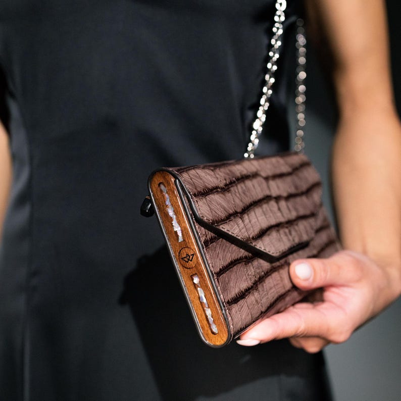 May include: A brown leather clutch purse with a wooden frame and a silver chain strap. The purse has a textured, striped pattern.