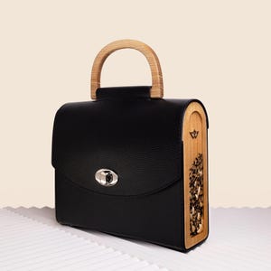 Bolso con asa superior y múltiples opciones de transporte. Bolso negro atemporal. Detalles de madera en los laterales. Elegante bolso de mano con flores secas naturales