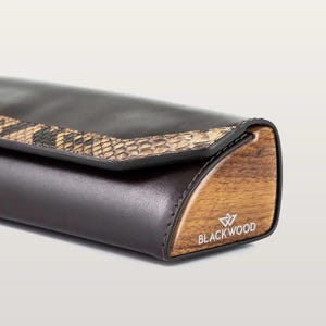 May include: A dark brown leather glasses case featuring a textured snakeskin pattern accent on the flap. The side panel is made of polished wood with the text BLACKWOOD and a geometric logo printed in white on the side.