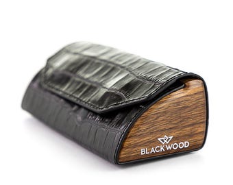 May include: A black, textured, rectangular case with a wooden end. The case has a flap closure and the brand name "BLACKWOOD" is printed in white on the wooden end. The case appears to be made of leather.