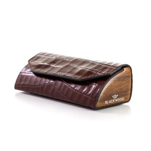 May include: A brown, crocodile-effect case with a wooden base. The case features a curved design and a flap closure. The brand name "BLACKWOOD" is printed on the wooden base.