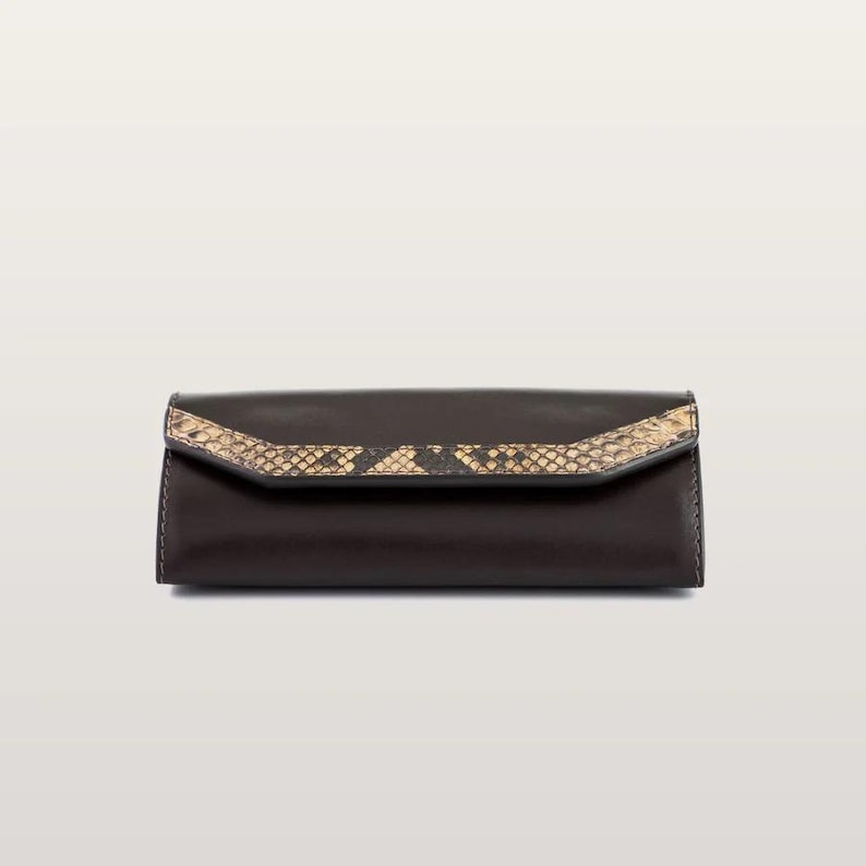 May include: A dark brown rectangular clutch with a smooth finish and a pointed flap closure. The flap features a textured, tan and black snakeskin-patterned inlay that runs horizontally across the center of the front panel.