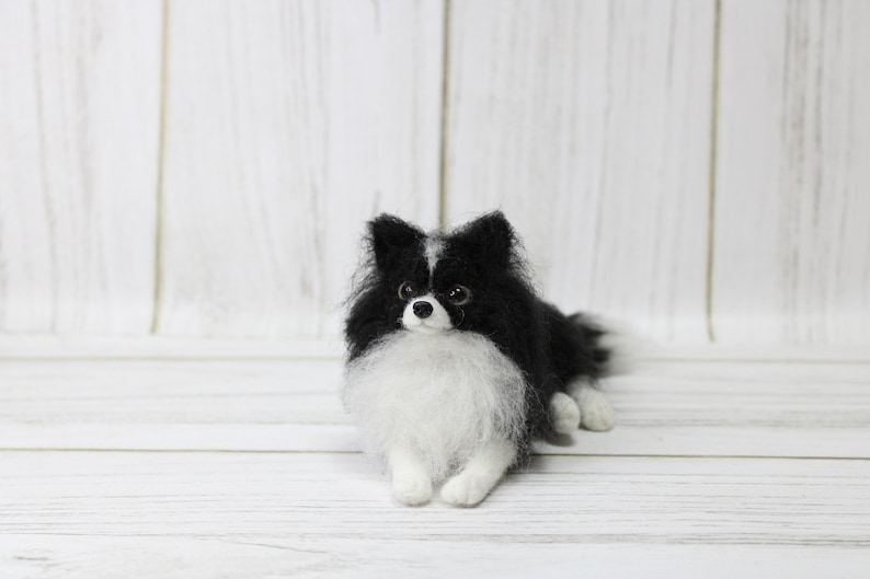 K&ouml;nnte beinhalten: Eine schwarz-wei&szlig;e Nadelfilz-Hundefigur, die auf einer wei&szlig;en Holzoberfl&auml;che liegt. Der Hund hat eine wei&szlig;e Brust und einen schwarzen Kopf mit schwarzen Ohren und einer wei&szlig;en Schnauze.