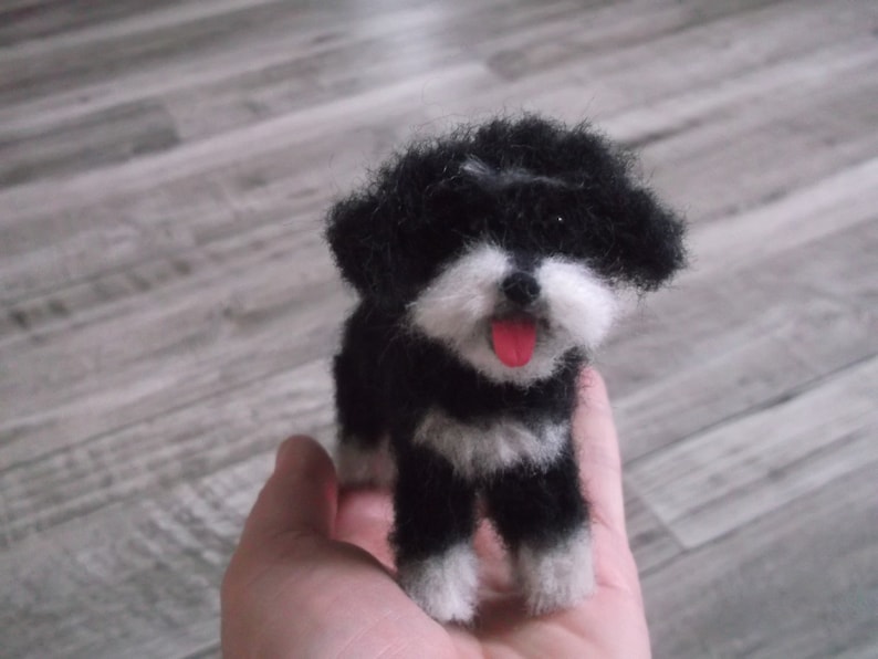 K&ouml;nnte beinhalten: Ein schwarz-wei&szlig;er Nadelfilz-Hund mit einer rosa Zunge, die herausragt. Der Hund steht auf einer Hand.