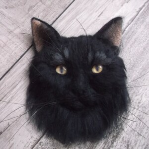 Puede incluir: Un gato negro con ojos amarillos, hecho de fieltro de aguja y presentado sobre una superficie de madera.