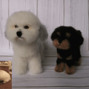 K&ouml;nnte beinhalten: Zwei Filz-Hundefiguren, eine wei&szlig;e mit grauen Ohren und eine schwarze mit braunen Akzenten. Die Figuren stehen auf einer wei&szlig;en Holzoberfl&auml;che.