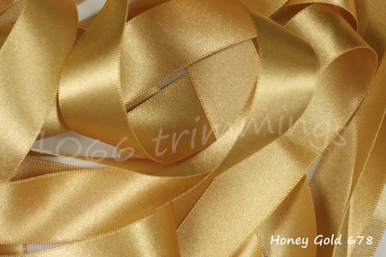May include: A close-up of a spool of honey gold satin ribbon. The ribbon is soft and shiny, with a subtle sheen. Honey Gold 678.