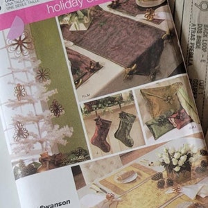 Op de afbeelding: Een Simplicity naaipatroon voor kerstversiering, patroonnummer 4313. Het patroon bevat instructies voor het maken van een tafelkleed, een kerstboom en een set kousen. Het patroon is gedrukt op een witte achtergrond met groene en bruine accenten.