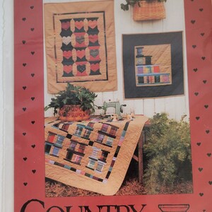 May include: A package featuring a quilt pattern with the text "SPOOLS" and "COUNTRY THREADS". The image shows three quilts with spool and heart designs, a sewing machine, and a basket of greenery.