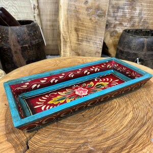 May include: A rectangular wooden tray with a red base and a turquoise border. The tray is decorated with hand-painted floral designs in shades of red, yellow, green, and pink.