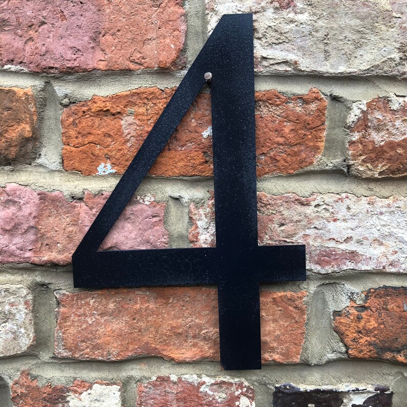May include: Black metal house number four attached to a brick wall.