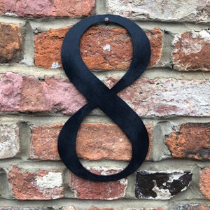 May include: Black metal number eight, attached to a brick wall. The number is made of a single piece of metal and has a simple, modern design.