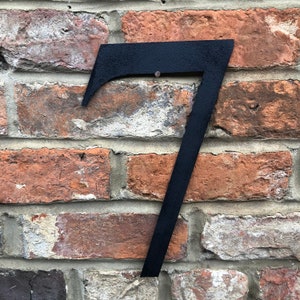 May include: Black metal house number seven attached to a brick wall.