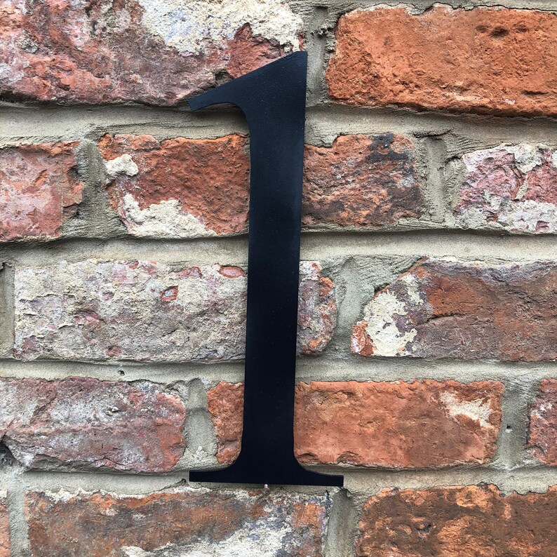 May include: Black metal house number one, mounted on a brick wall.