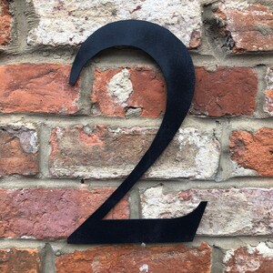 May include: Black metal number two attached to a brick wall.