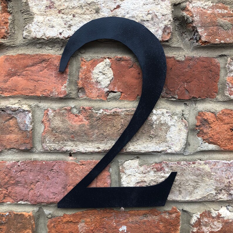 May include: Black metal number two attached to a brick wall.