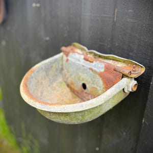 May include: A rusty metal trough for animals to drink from, mounted on a dark wooden wall.