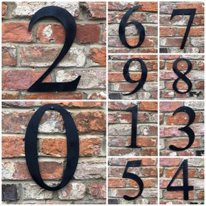 May include: A set of black metal house numbers, 0 through 9, displayed on a brick wall. Each number is individually mounted and has a rustic, industrial look.