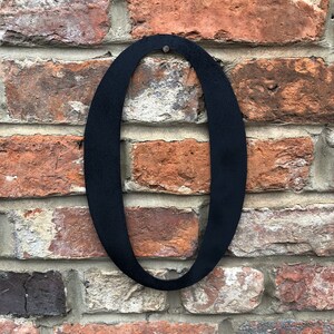 May include: Black metal number zero, mounted on a brick wall.