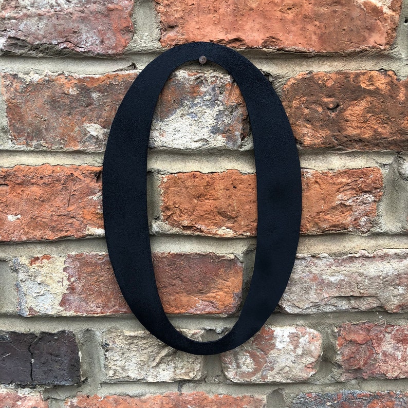 May include: Black metal number zero, mounted on a brick wall.