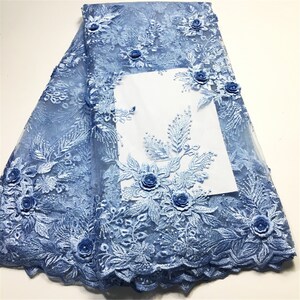 Puede incluir: Tela de encaje azul claro con aplicaciones florales 3D. La tela tiene una textura de malla delicada y presenta diseños florales intrincados con detalles en relieve.