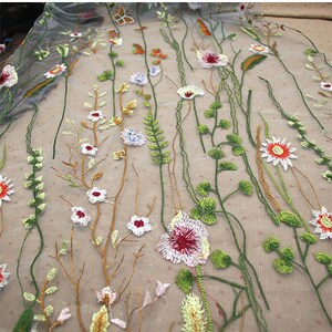 K&ouml;nnte beinhalten: Nahaufnahme eines bestickten floralen Stoffes. Der Stoff weist ein zartes Muster aus verschiedenen Blumen und Bl&auml;ttern in Wei&szlig;, Rot, Orange und Gr&uuml;n mit braunen Stielen und Bl&auml;ttern auf. Der Hintergrund ist hellbeige.