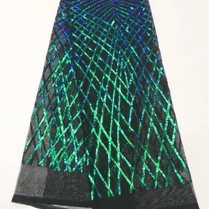 Op de afbeelding: Groene en blauwe iriserende pailletten op een zwart mesh-stof. De pailletten zijn gerangschikt in een geometrisch patroon.