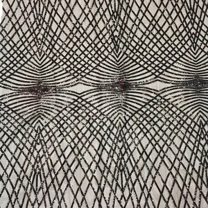 Op de afbeelding: Zwarte en zilveren paillettenstof met een geometrisch patroon. De stof heeft een mesh-rug.
