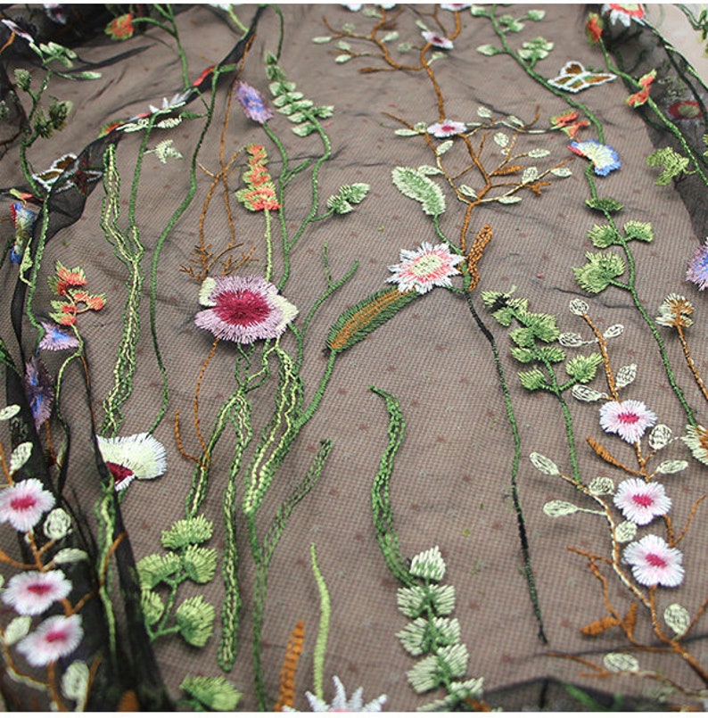 K&ouml;nnte beinhalten: Nahaufnahme eines schwarzen, transparenten Stoffes mit gesticktem Blumendesign. Die Stickerei zeigt eine Vielzahl farbenfroher Blumen, darunter rosa, wei&szlig; und lila, mit gr&uuml;nen Stielen und Bl&auml;ttern. Der Stoff hat ein gepunktetes Muster.