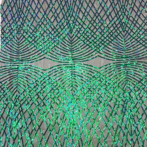 Op de afbeelding: Groene en blauwe iriserende pailletten op een mesh-stof. De pailletten zijn gerangschikt in een geometrisch patroon van elkaar kruisende lijnen en curves.