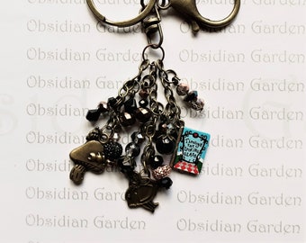 May include: A charm bracelet with a gold-tone chain and various charms, including a miniature book with the text "Through the Looking Glass", a mushroom, a bird, and black and brown beads.