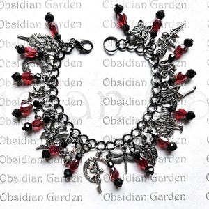 May include: A silver charm bracelet with red and black beads. The charms include a crescent moon, a butterfly, and a dragonfly. The bracelet is on a white background with the text "Obsidian Garden" repeated.