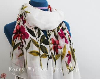 May include: White scarf with a floral print featuring pink, red, and green flowers. The scarf has white tassels on the ends.