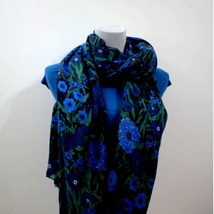 Pode incluir: Um cachecol azul e verde com padrão floral sobre um fundo azul escuro. O cachecol está amarrado ao redor do pescoço de um manequim.