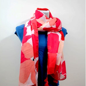 May include: A pink and white floral print scarf with tassels. The scarf is draped over a blue shirt.