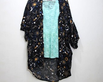 May include: A black kimono with a celestial print featuring stars, moons, and suns. The kimono has a long, flowing silhouette and is made of a lightweight fabric. It is paired with a light blue lace top.