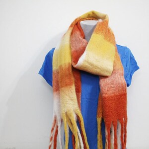 May include: A long, orange, yellow, and white striped scarf with fringe on the ends.