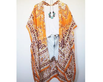 May include: Orange and white patterned kimono with a paisley design. The kimono is worn over a white t-shirt and denim shorts.