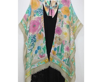 May include: A floral print kimono with a light beige background and a black lace trim. The kimono has a V-neck and is open in the front. It features a turquoise and silver necklace.
