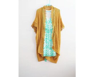 May include: A mustard yellow crochet cardigan with a lace trim. The cardigan is open in the front and has a light blue and white patterned dress underneath.