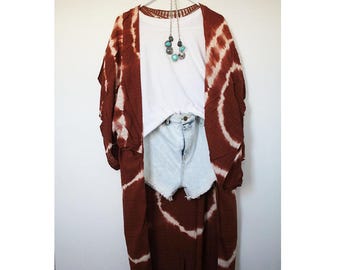May include: A long, brown tie-dye kimono with white accents. The kimono is open in the front and has a white t-shirt and denim shorts underneath.