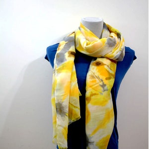 May include: A yellow and gray scarf with a tie-dye pattern. The scarf is draped over a mannequin wearing a blue shirt.