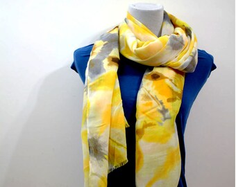 May include: A yellow and gray scarf with a tie-dye pattern. The scarf is draped over a mannequin wearing a blue shirt.