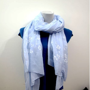Könnte beinhalten: Ein hellblauer Schal mit weißem Blumenmuster. Der Schal ist aus weichem, leichtem Stoff gefertigt und perfekt, um jedem Outfit einen Hauch von Eleganz zu verleihen.